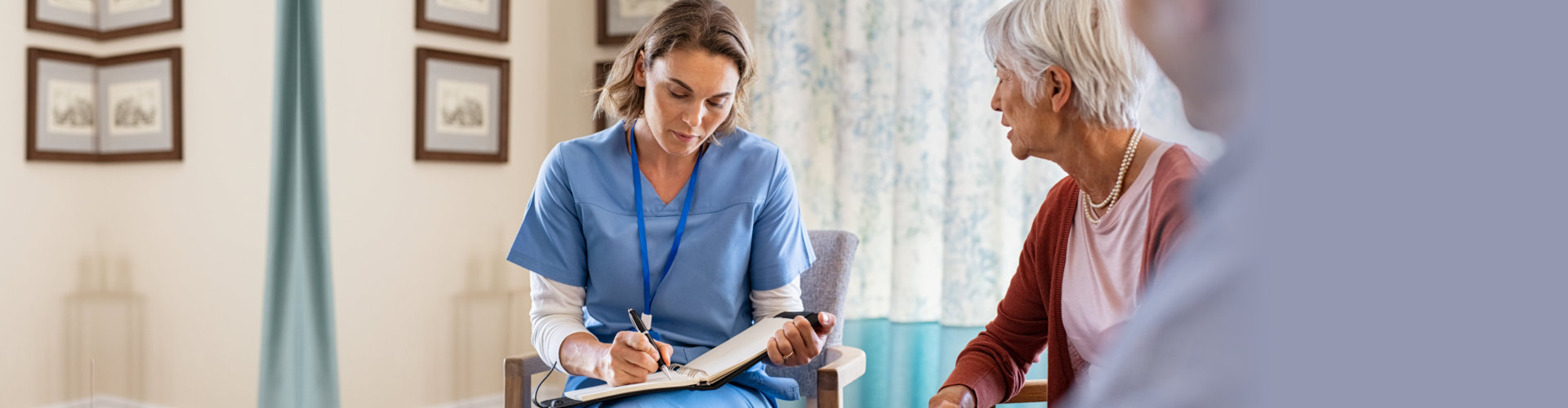 Nurse talking to old patients while being in a nursing home. Young healthcare worker visiting senior couple at care centre and writing information. Nurse wearing uniform noting symptoms of elderly woman
